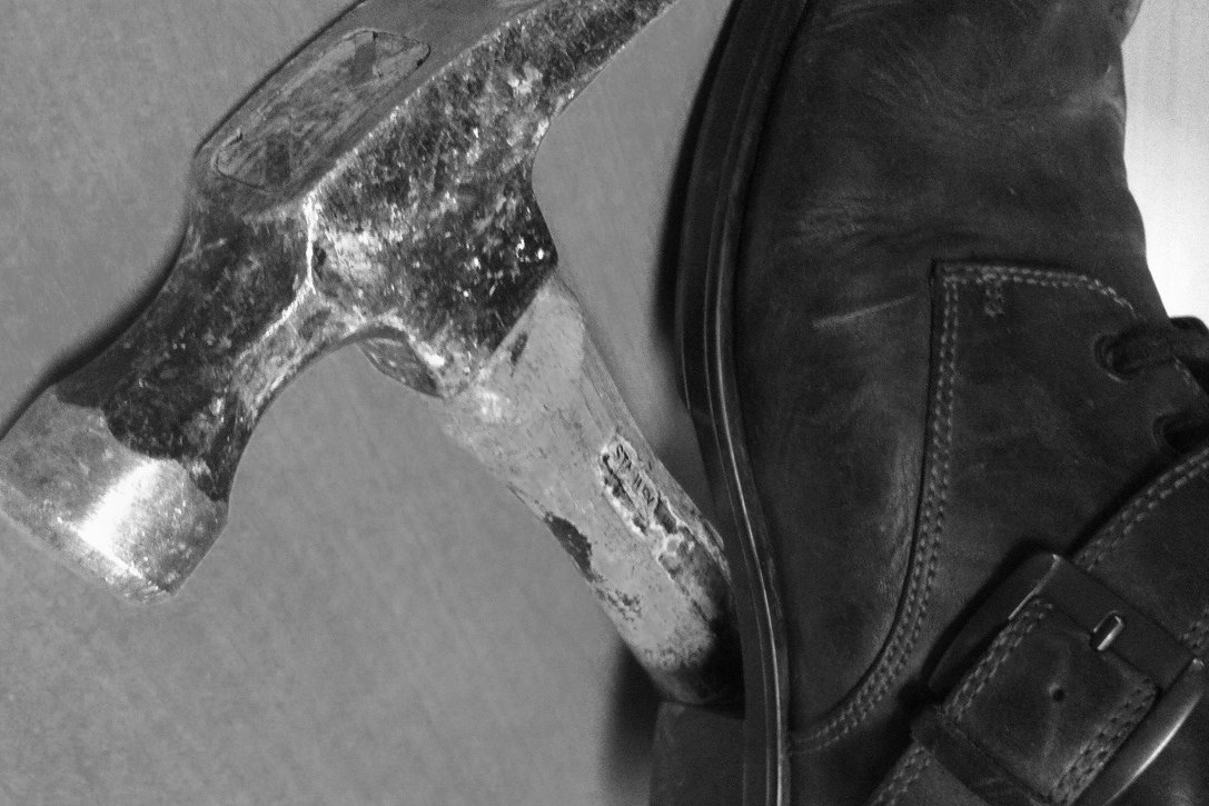 A claw hammer resting against a black leather boot